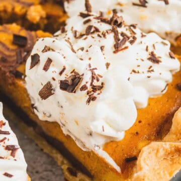 Close-up of pumpkin pie slices topped with whipped cream and chocolate shavings in a pie dish.