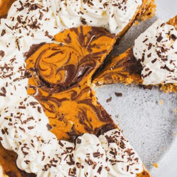 Pumpkin pie topped with whipped cream and chocolate shavings, with one slice slightly removed from the dish.