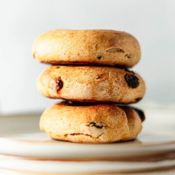 Three golden-brown bread rolls with raisins stacked on a plate against a light background.