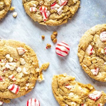 Cookies with white chocolate chips and crushed peppermint candy on parchment paper, with whole candies visible.