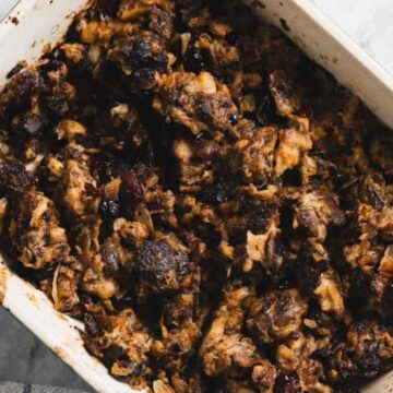 A white baking dish filled with dark, rustic bread pudding on a marble surface.