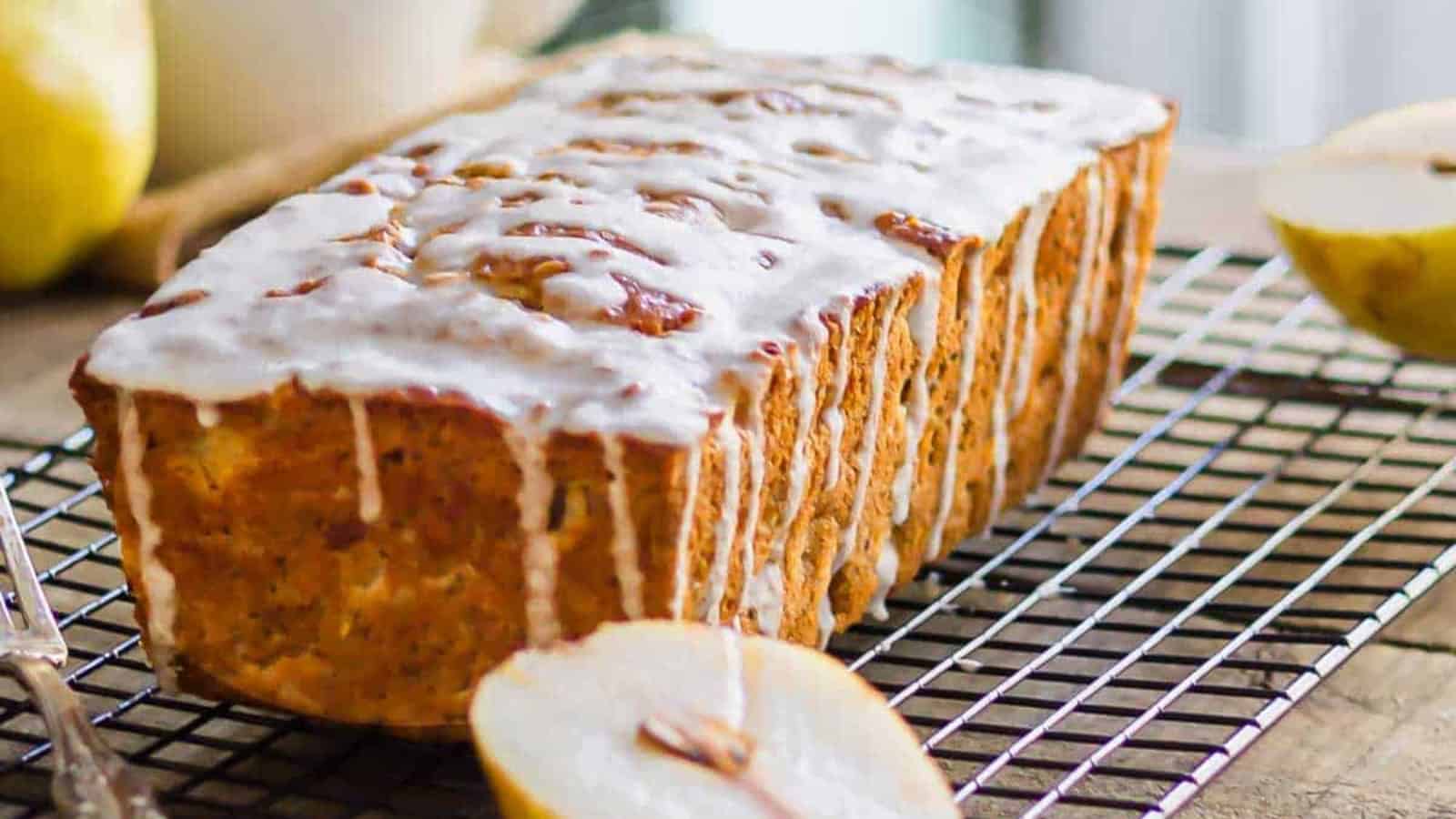 Granola pear bread with icing sliced on a cooling rack.