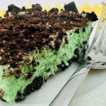A slice of mint Oreo pie with a creamy green filling and chocolate cookie crumbs on a white plate with a fork.
