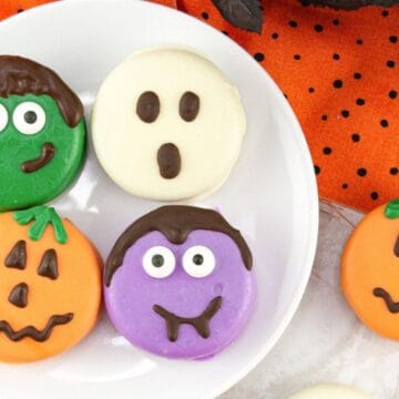 Four Halloween-themed cookies on a white plate, decorated as a ghost, Frankenstein, and two jack-o'-lanterns.
