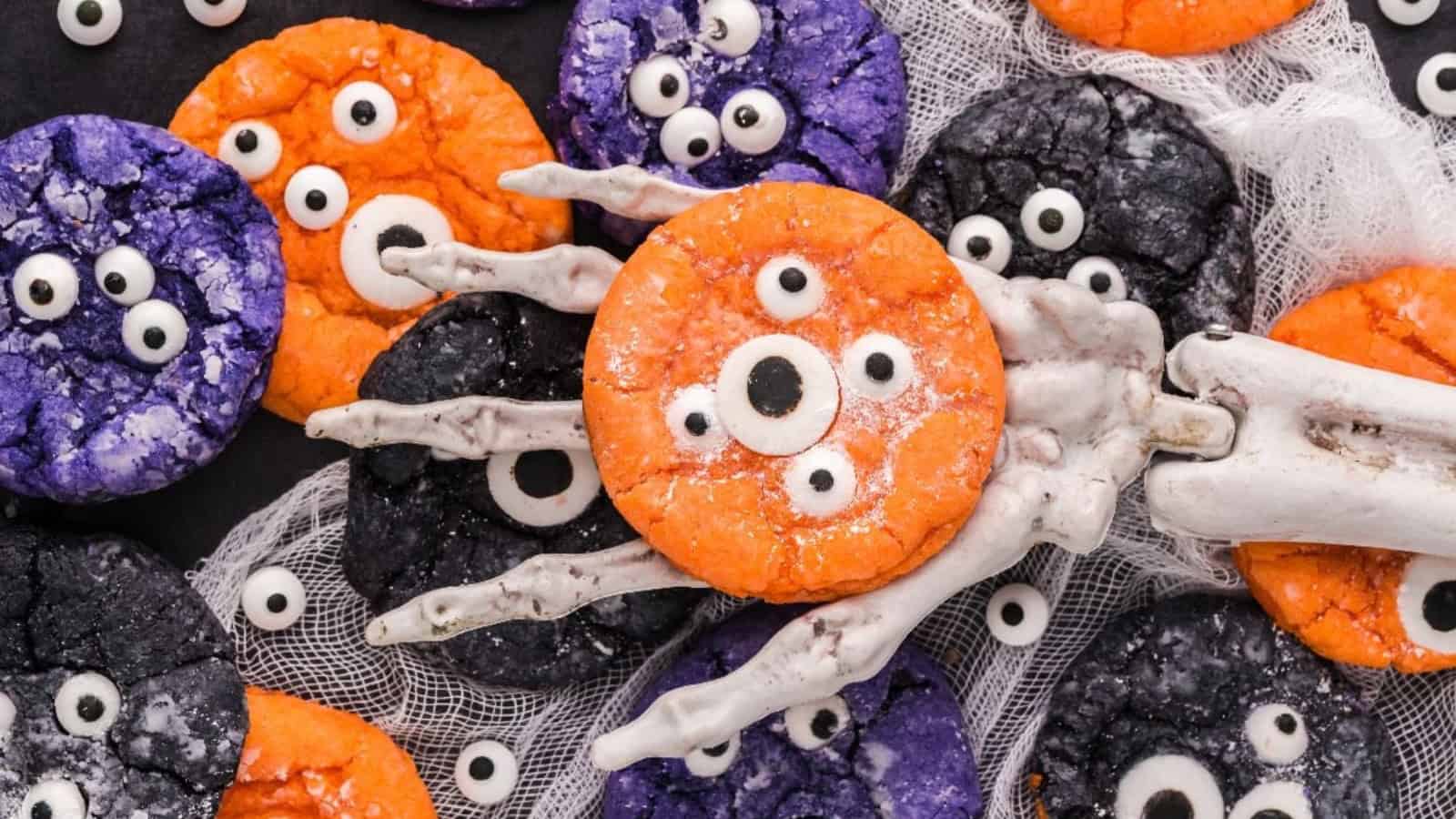 Colorful Halloween crinkle cookies in orange, purple, and black decorated with candy eyes and a skeleton hand prop.