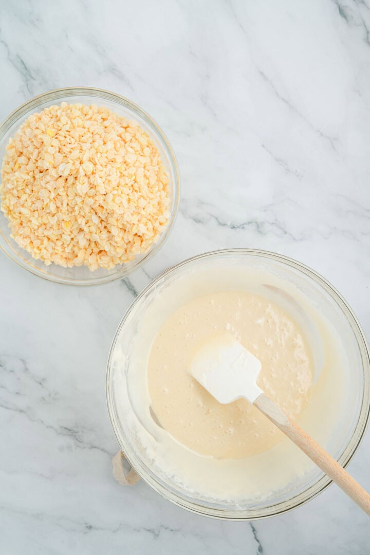 A bowl of yellow lentils sits next to a bowl of batter with a spatula on a marble surface, ready for baking delicious treats like Halloween Candy Rice Krispies.