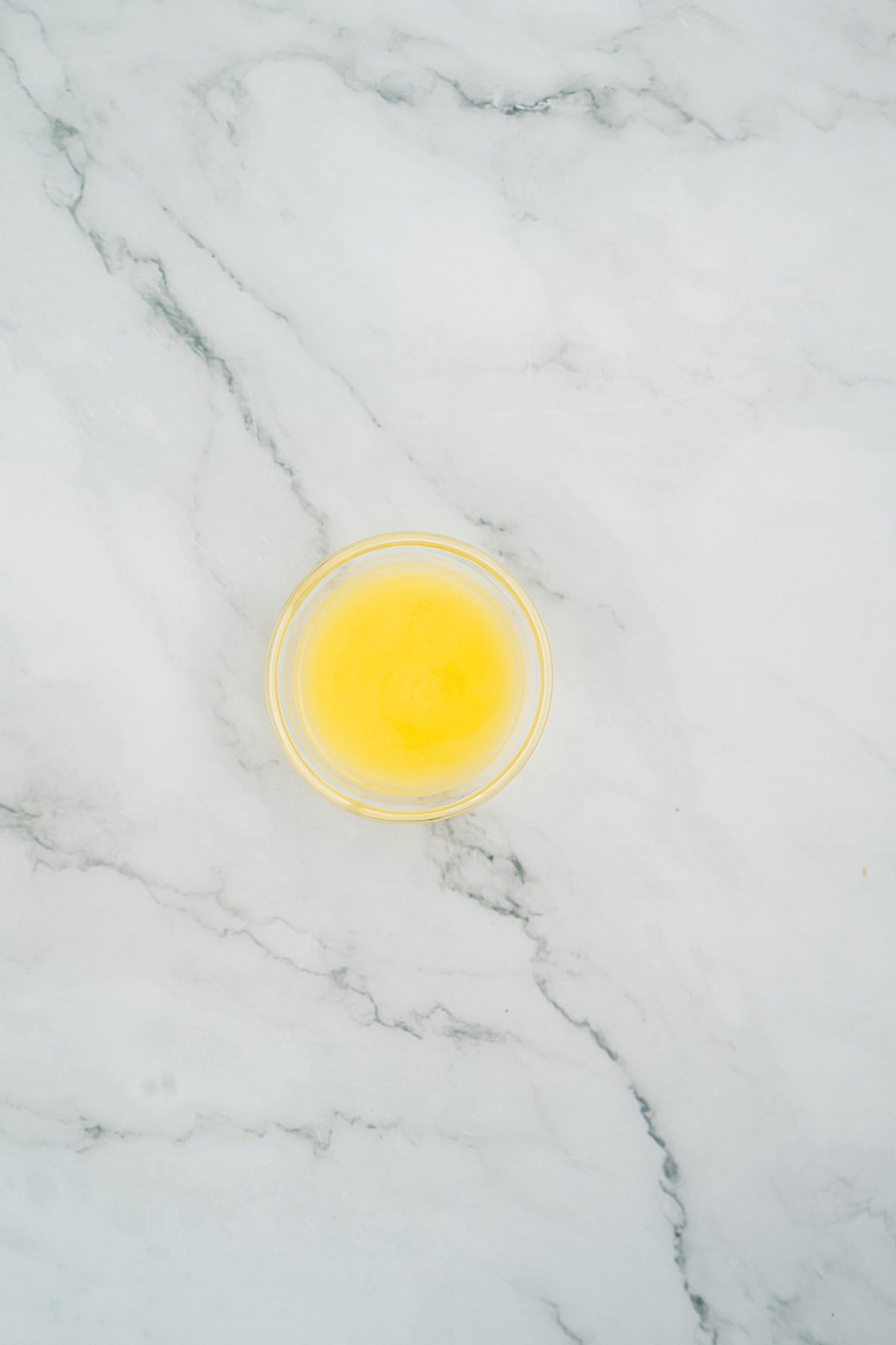 A small bowl of melted butter on a white marble surface, ready to be mixed into Halloween Candy Rice Krispies.