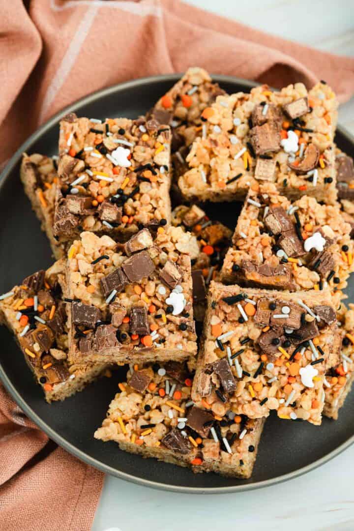A plate of Halloween Candy Rice Krispies treats topped with chocolate pieces and colorful orange, black, and white sprinkles.