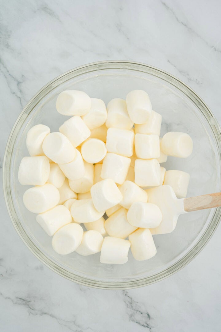 A glass bowl filled with white marshmallows and a spatula on a marble surface, ready for making Halloween Candy Rice Krispies.