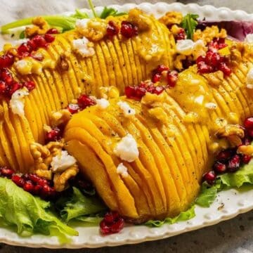 Sliced roasted squash on greens, topped with pomegranate seeds, walnuts, and crumbled cheese.