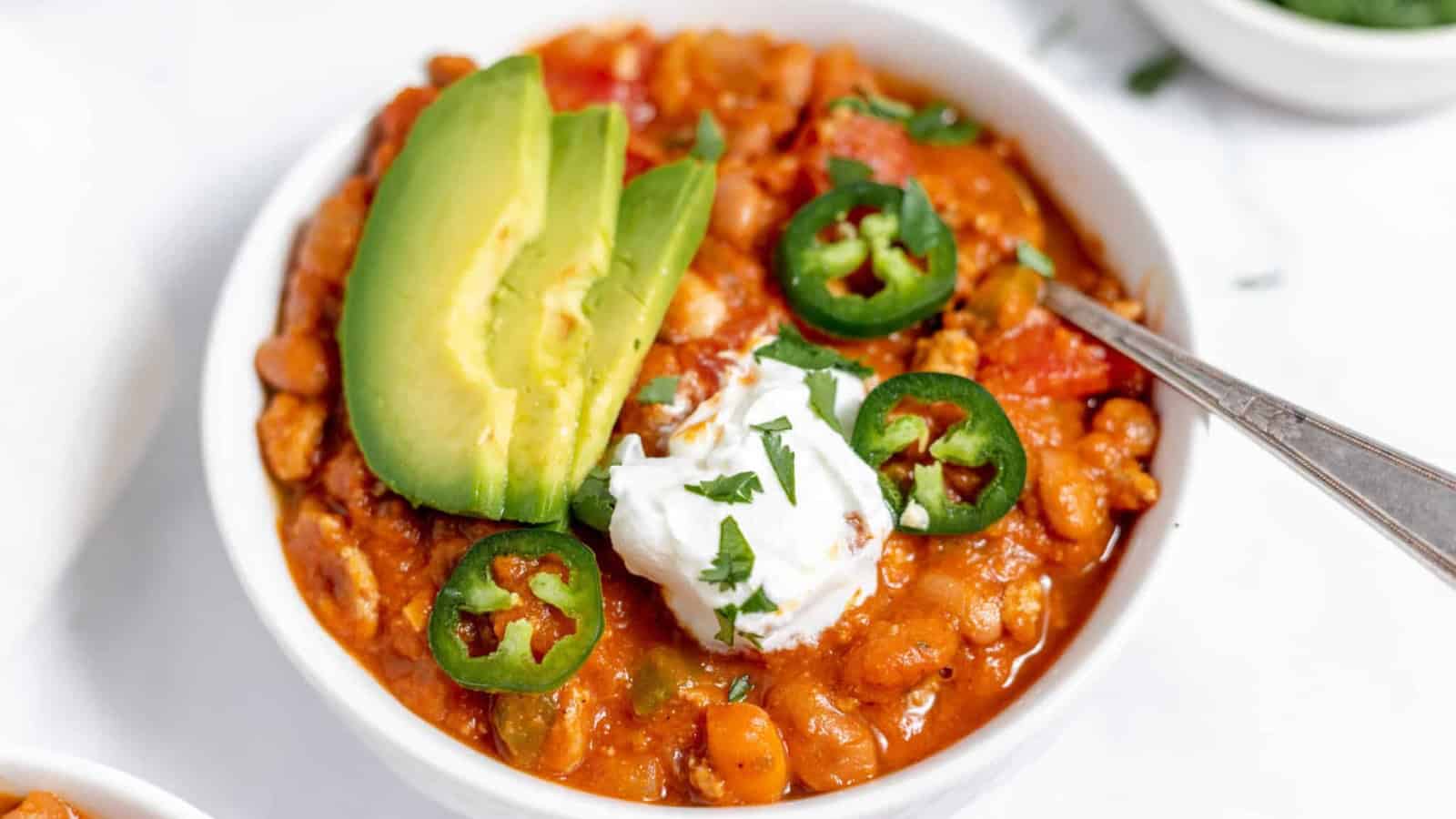 A bowl of chili topped with avocado and peppers.