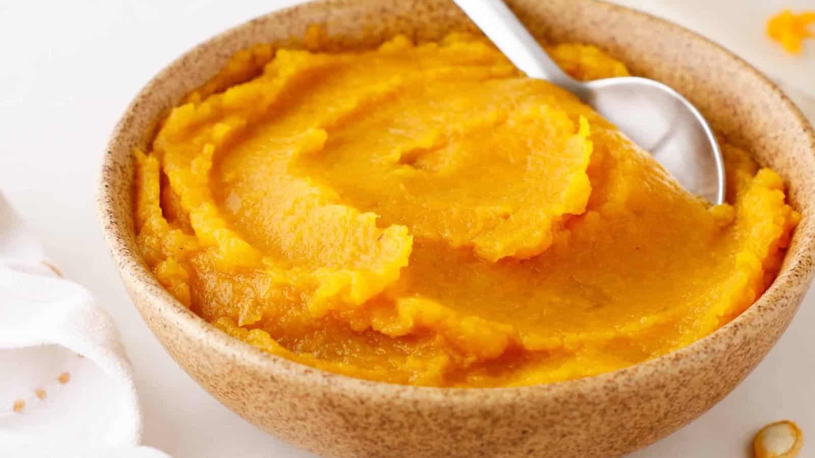 A bowl of smooth, orange pumpkin puree with a spoon resting inside.