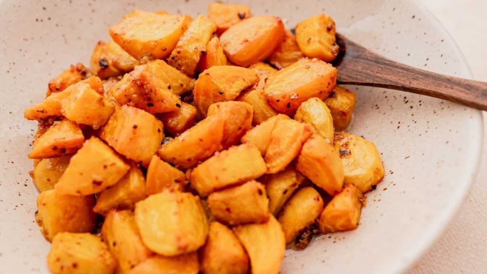 A bowl of roasted, golden-brown sweet potatoes with a wooden spoon.
