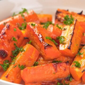 Roasted carrot sticks garnished with chopped parsley in a white dish.