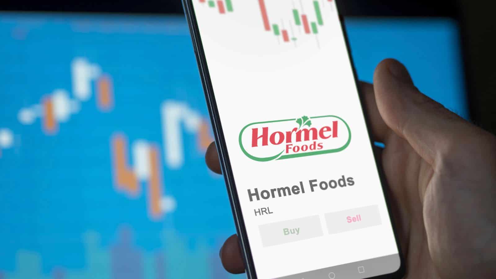 A phone displays Hormel Foods stock info with buy and sell options; graphs are blurred in the background.