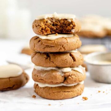 A stack of frosted cookies, one with a bite taken out, with more cookies and frosting in the background.