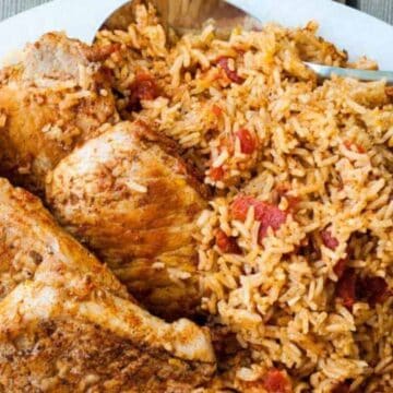 A plate of seasoned rice with tomatoes and three pieces of cooked pork chops, served with a spoon.