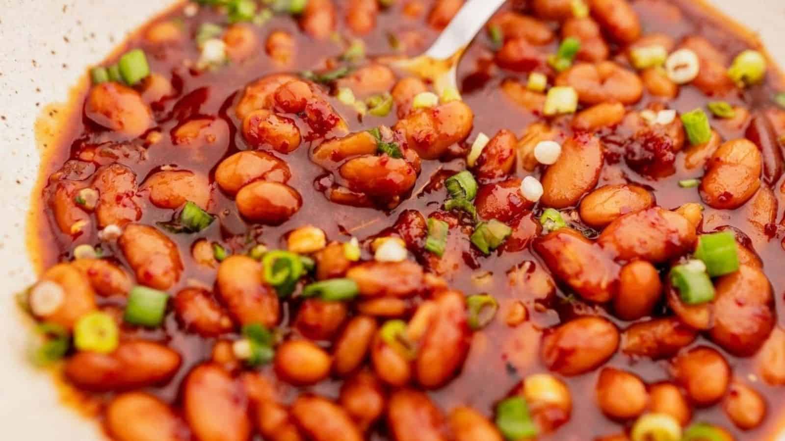 A bowl of spicy beans in sauce, garnished with chopped green onions and a spoon.
