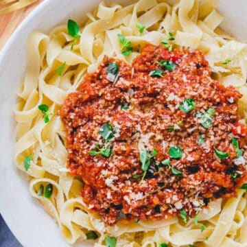 A bowl of fettuccine pasta topped with meat sauce and fresh herbs, with grated cheese on the side.