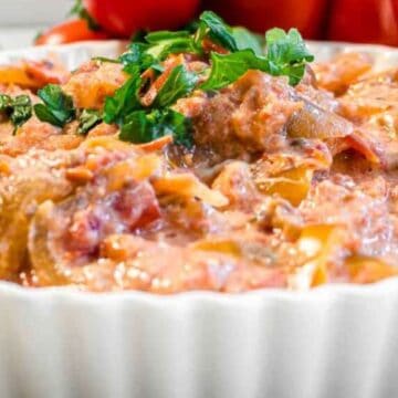 A creamy tomato-based dip garnished with fresh parsley in a white dish, with tomatoes in the background.