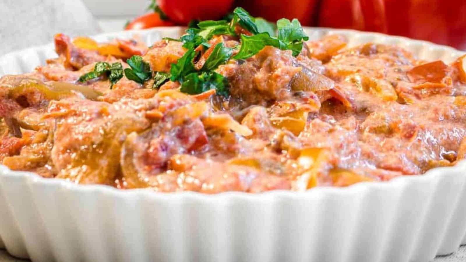 A creamy tomato-based dip garnished with fresh parsley in a white dish, with tomatoes in the background.