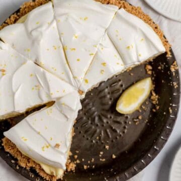 A creamy lemon pie with a crumbly crust, topped with lemon zest, sliced and served with lemon wedges.