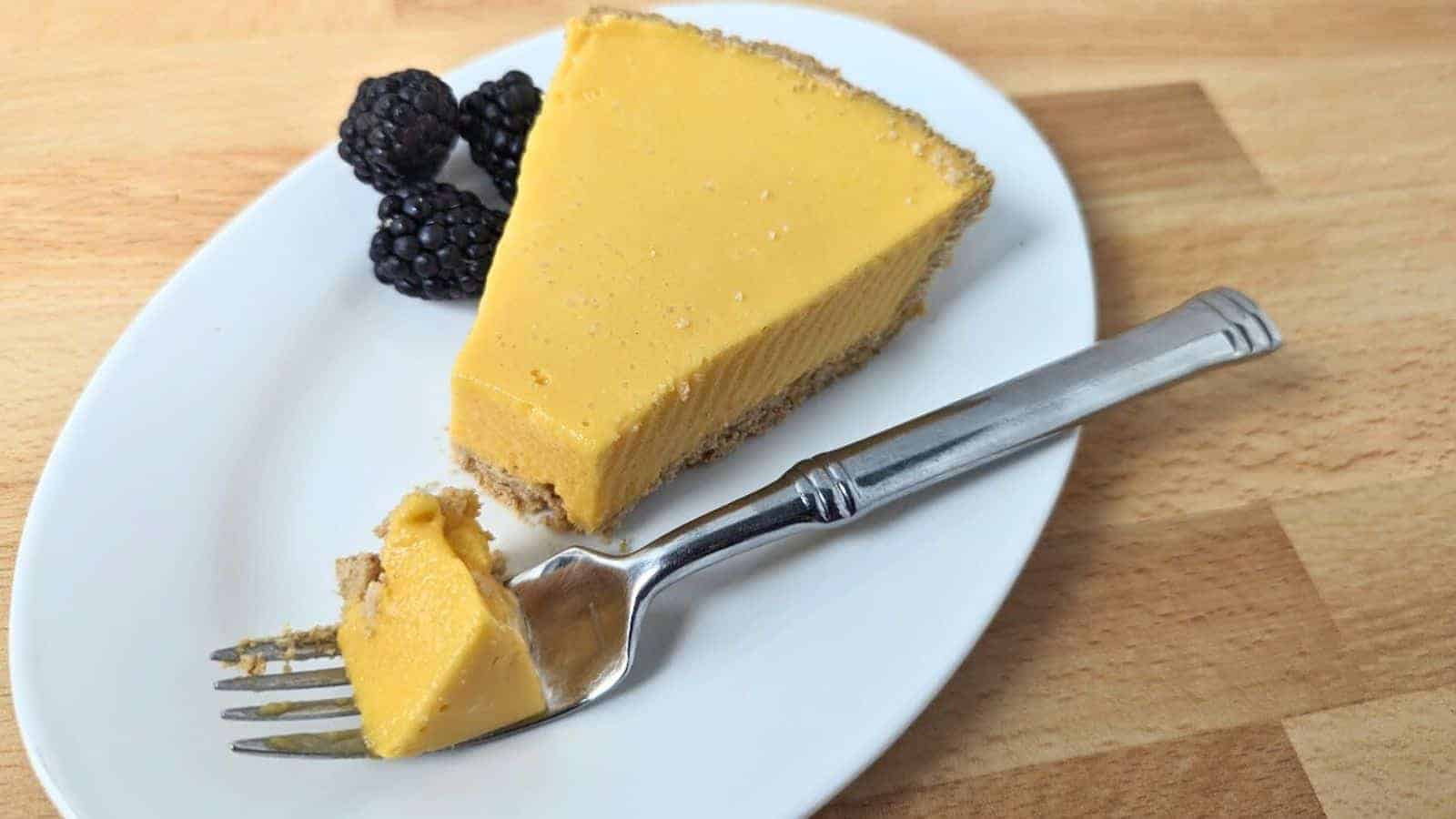 Image shows a slice of mango pie on a white plate with three blackberries and a fork holding a small piece of pie.