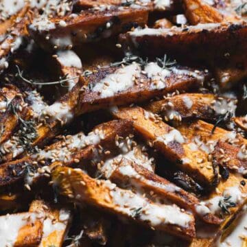 Sweet potato fries topped with a creamy white sauce, herbs, and sesame seeds on a baking tray.