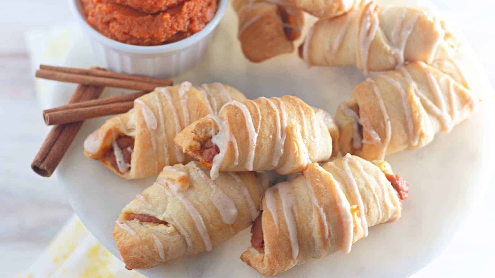 Mini pumpkin crescent rolls with dipping sauce on a plate.