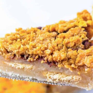 A close-up of a slice of pie with a golden crumb topping and flaky crust on a metal spatula.