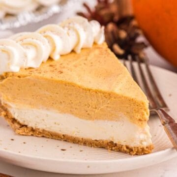 A slice of pumpkin cheesecake pie with whipped cream on a plate, next to a fork and pumpkin.