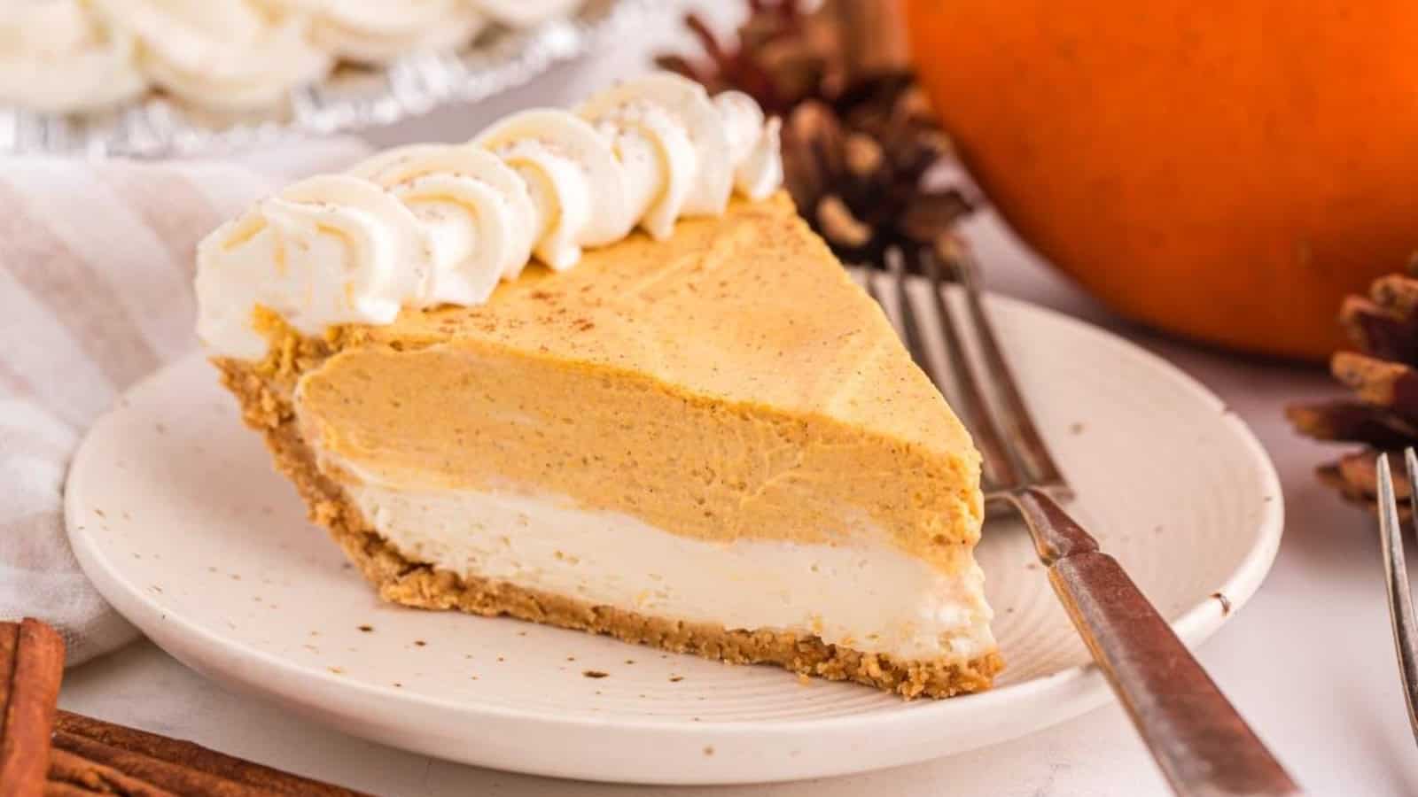 A slice of pumpkin cheesecake pie with whipped cream on a plate, next to a fork and pumpkin.