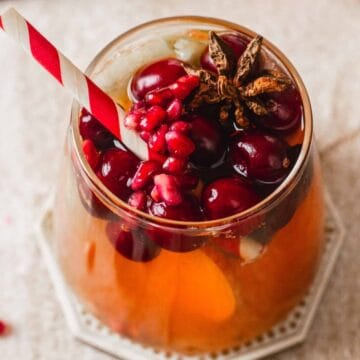 A festive drink garnished with cranberries, pomegranate seeds, ice, and a striped straw in a glass.