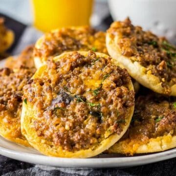 Small round mini pizzas topped with seasoned ground meat and cheese, served on a white plate.