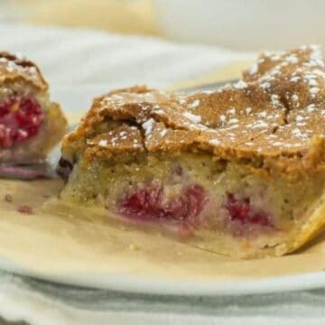 A slice of berry pie with a golden crust and a dusting of powdered sugar on a white plate.