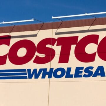 The Costco Wholesale logo on the exterior wall of a store against a clear blue sky.