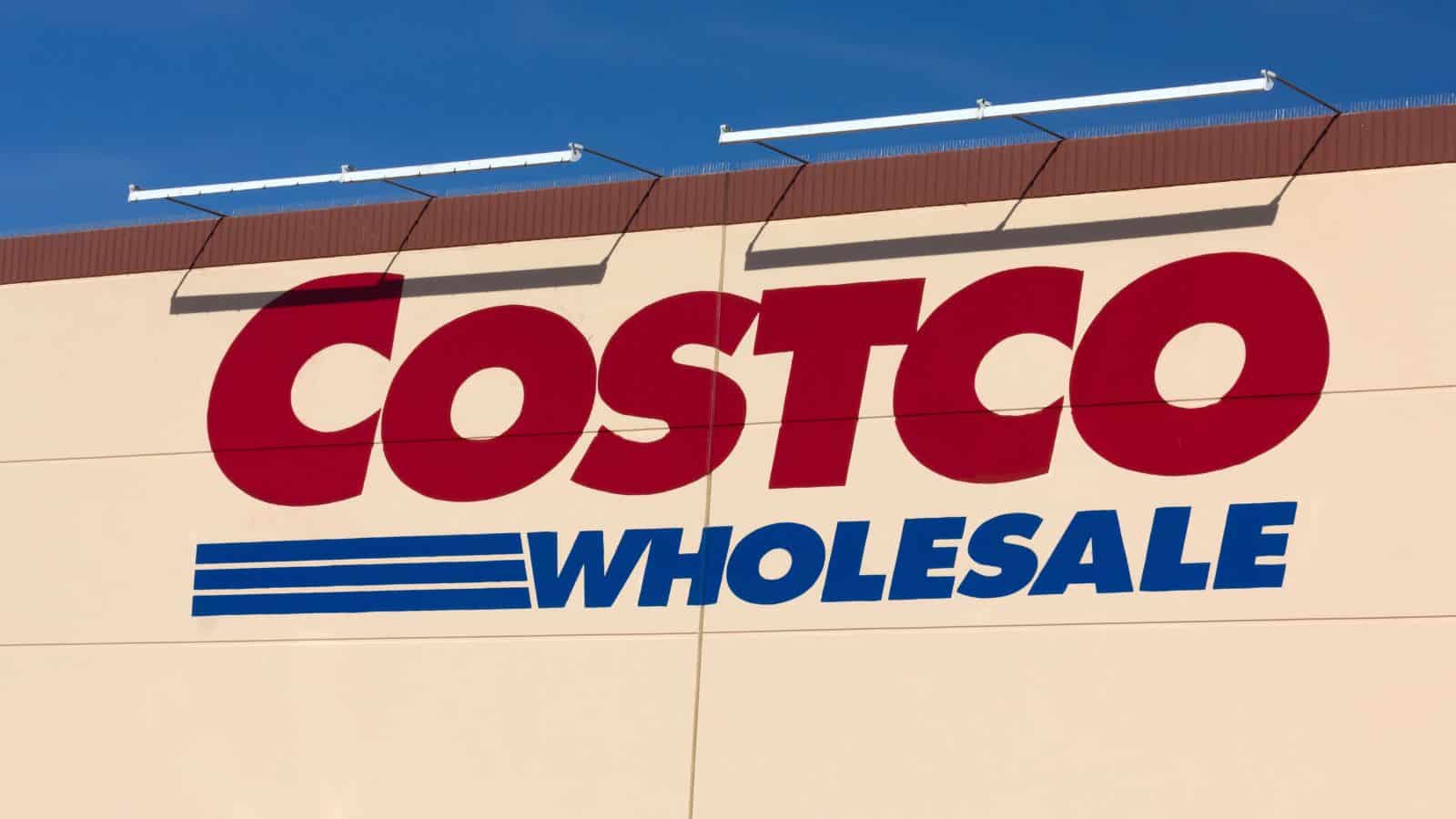 The Costco Wholesale logo on the exterior wall of a store against a clear blue sky.