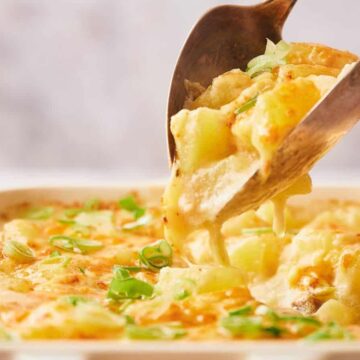 Close-up of cheesy scalloped potatoes being served from a baking dish, topped with chopped green onions.