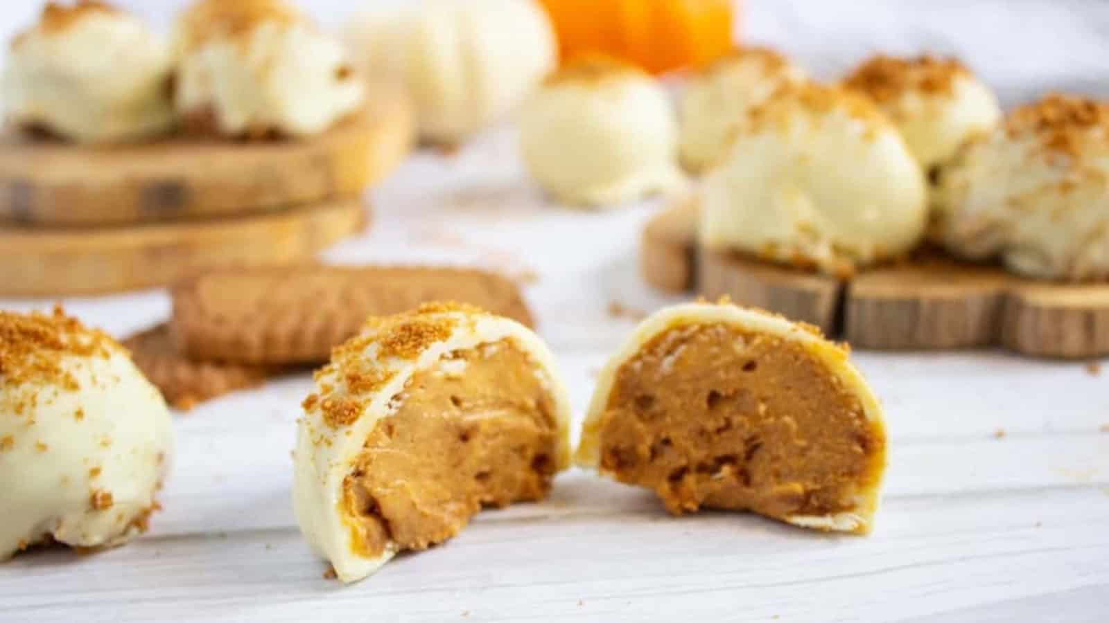 White chocolate pumpkin truffle topped with cookie crumbs, next to whole cookies on a white wooden surface.