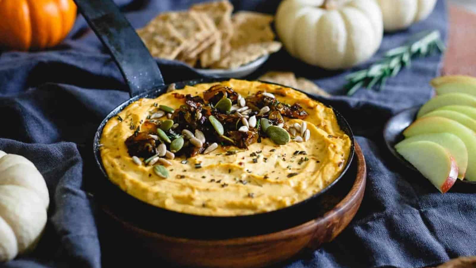 Pumpkin goat cheese dip topped with caramelized onions, sunflower seeds and pepitas in a small skillet.