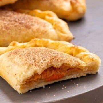 Close-up of a baked empanada with a bite taken out, showing a sweet filling and cinnamon sugar topping.