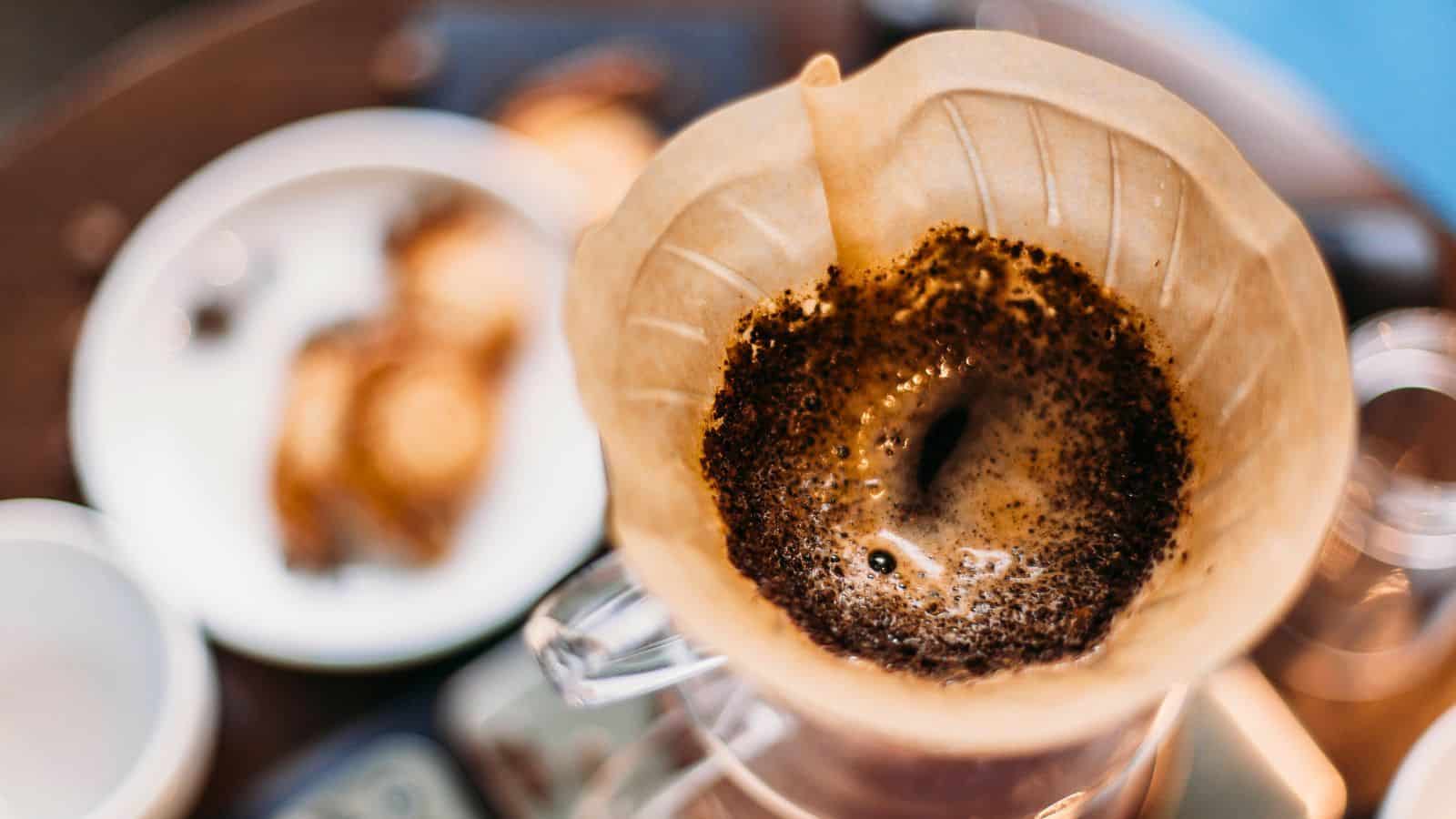 Coffee brewing in a pour-over filter with ground coffee, with blurred pastries in the background.