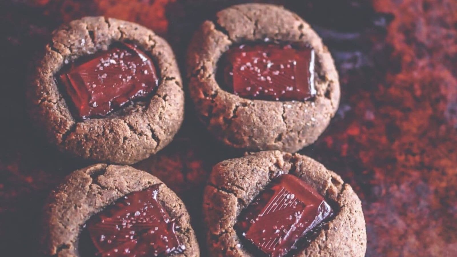 Four chocolate thumbprint cookies with a piece of chocolate in the center, sprinkled with sea salt.