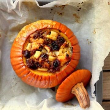 Baked stuffed pumpkin filled with a savory mixture, placed on parchment in a baking dish, with lid beside it.
