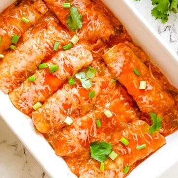 Baked enchiladas topped with red sauce, melted cheese, green onions, and cilantro in a white dish.
