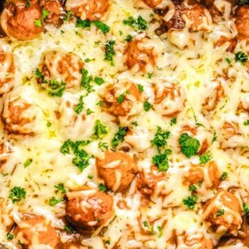 Meatballs topped with melted cheese and chopped parsley in a slow cooker.