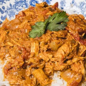 Shredded chicken in a tomato-based sauce served over white rice, garnished with cilantro on a blue patterned plate—an ideal option for delicious leftover recipes.