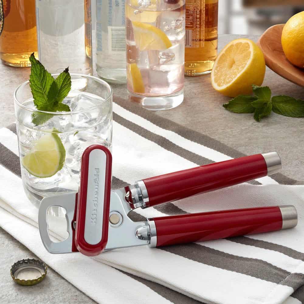 Red-handled bottle opener—one of the essential cooking tools for beginners—rests on a striped towel beside a glass of ice water with lime and mint, and a fresh lemon.