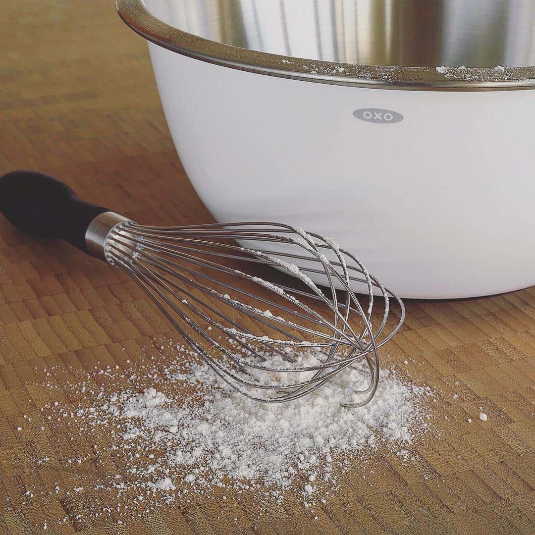 A whisk with flour beside a mixing bowl on a wooden surface, these essential cooking tools for beginners make baking easy and enjoyable.