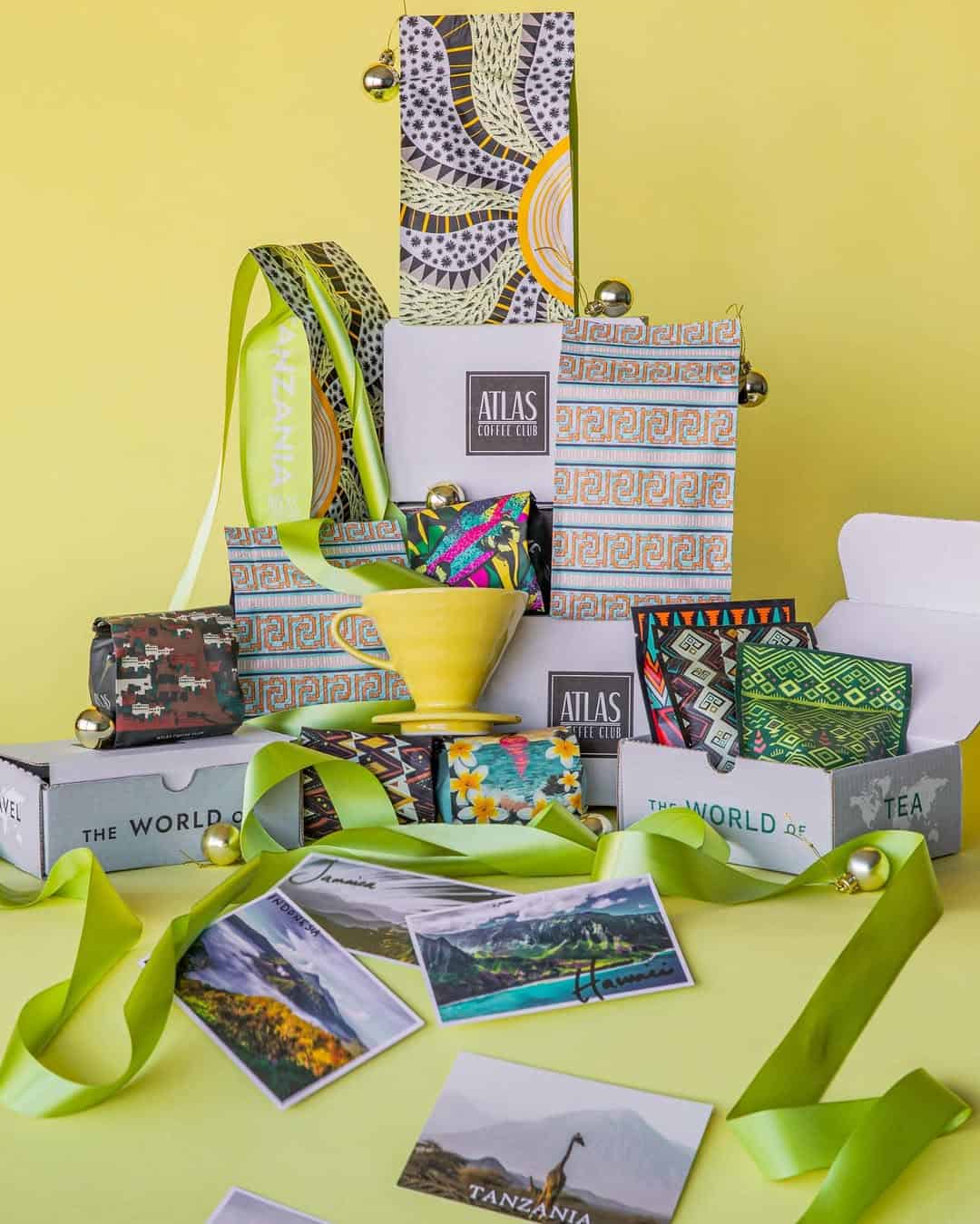 Gift boxes with patterned designs, postcards, green ribbons, and a yellow cup arranged on a yellow background.